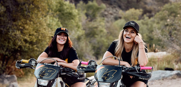 two girls sitting on dirtbikes wearing hats