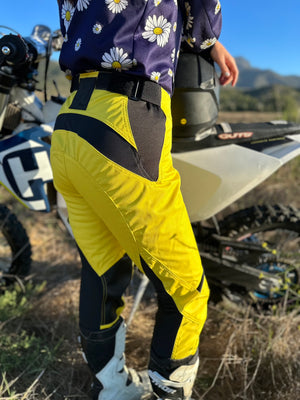 Woman standing next to her dirt bike wearing a navy blue and daisy dirt bike jersey and bright yellow womens dirt bike pants