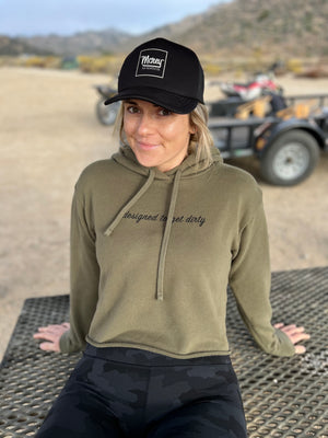 Woman wearing an army green cropped hoodie with the words designed to get dirty across the front.