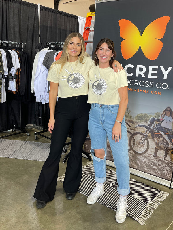 Two women standing next to each other wearing the He Loves Me Not Crop Tee.