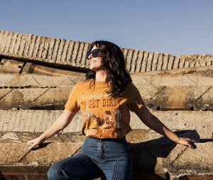 Woman wearing a mustard yellow t-shirt with text and graphics, sitting on a large piece of equipment.