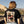 Load image into Gallery viewer, Person wearing a black t-shirt with a graphic design, standing outdoors with mountains in the background.
