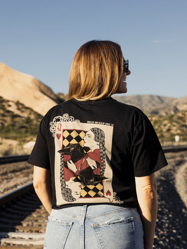 Person wearing a black t-shirt with a graphic design, standing outdoors with mountains in the background.