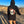 Load image into Gallery viewer, Woman wearing a black hoodie with a skull surrounded by flowers and butterflies on the back. She&#39;s watching people ride a dirt bike track.

