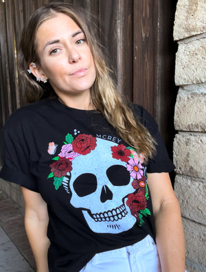 Woman wearing a black shirt with a skull surrounded by flowers and butterflies on the front.
