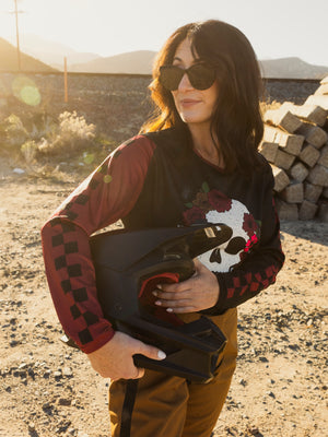 Woman holding a helmet in a desert-like setting with mountains in the background