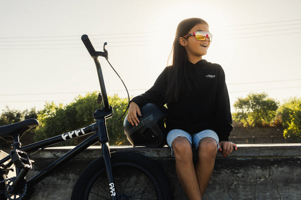 young girl sitting at a BMX park next to her bike, wearing a black hoodie with the words 'Designed to get dirty' on the front