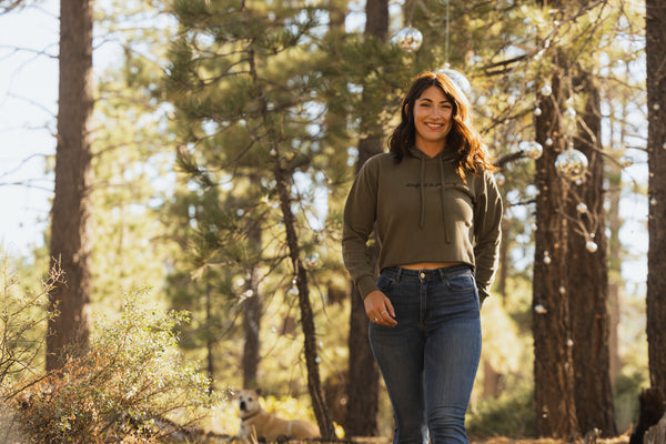 Woman wearing an army green cropped hoodie with the words designed to get dirty across the front.