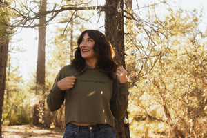 Woman wearing an army green cropped hoodie with the words designed to get dirty across the front.