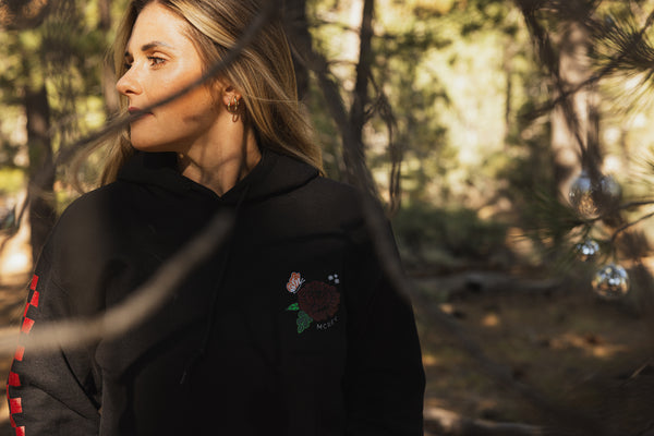 Woman wearing a black hoodie with a flower design on the front and red checkers down the sleeve.