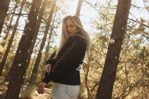 Woman wearing a black hoodie with a flower design on the front and red checkers down the sleeve.