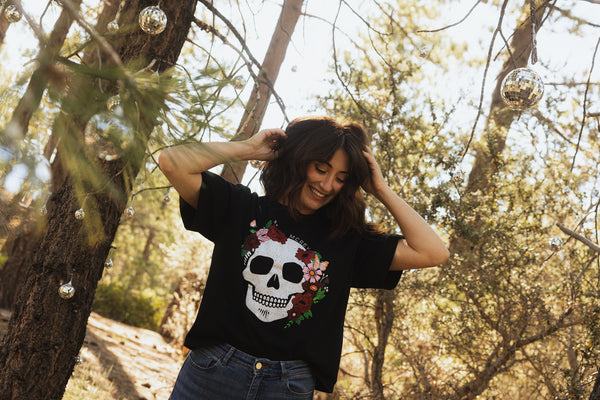 Woman wearing a black shirt with a flower skull on the front. She's dancing in the woods under a bunch of disco balls.