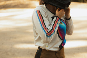 Woman strapping her helmet. She's wearing a 70's-inspired dirt bike jersey and mocha pants.