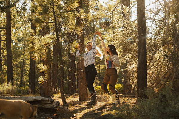 Two women dancing in the middle of the woods under disco balls. They are wearing women's dirt bike gear designed by MCREY MOTOCROSS CO.