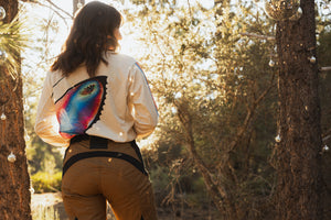 Woman standing in the woods wearing a pair of mocha and black dirt bike pants, and a 70's inspired jersey with a butterfly on it.