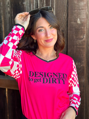 Woman wearing a hot pink dirt bike jersey with checkered sleeves and the words "Designed to get dirty®" across the front.