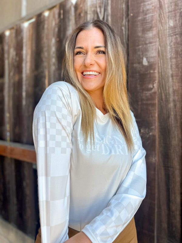 Woman wearing a off-white dirt bike jersey with checkered sleeves and the words "Designed to get dirty®" across the front.