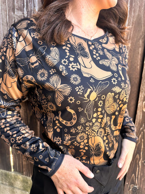 Woman wearing a cowgirl hat and a women's black dirt bike jersey with tan cowgirl boots, butterflies, horseshoes, and bees on it.