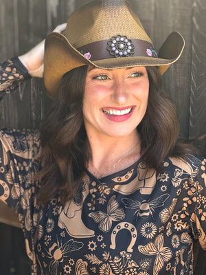 Woman wearing a cowgirl hat and a women's black dirt bike jersey with tan cowgirl boots, butterflies, horseshoes, and bees on it.
