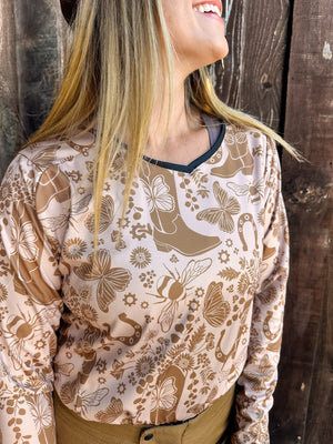 Woman wearing a women's tan dirt bike jersey with tan cowgirl boots, butterflies, horseshoes, and bees on it.