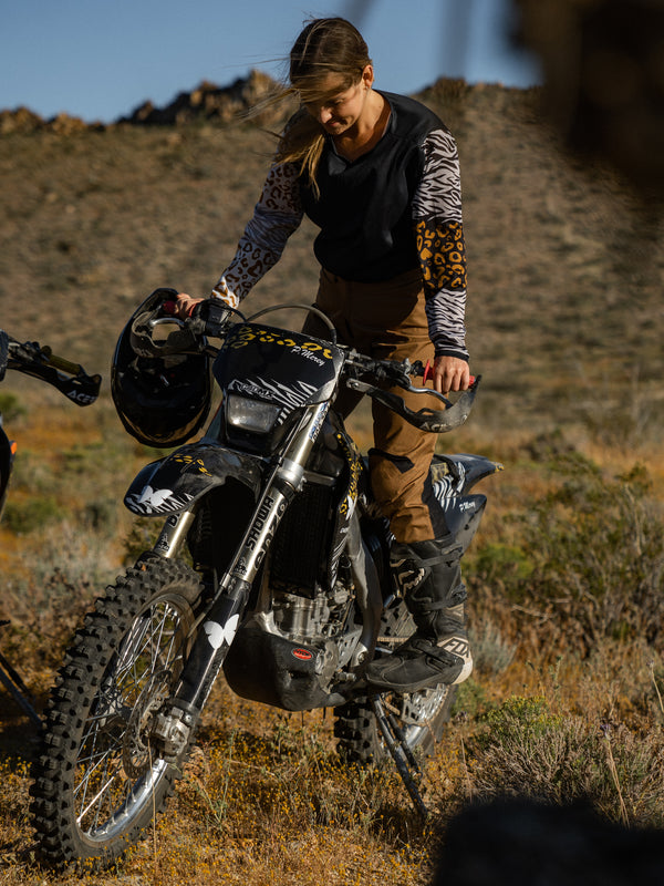 Woman standing on her dirt bike wearing mocha pants and a women's animal print dirt bike jersey.