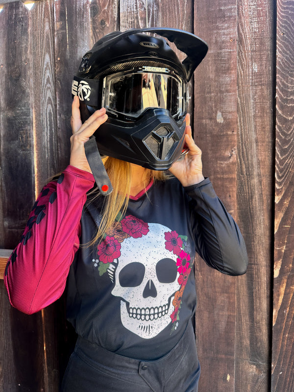 Person wearing a black helmet and black dirt bike jersey with a skull and flowers on the front.