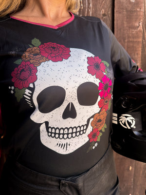 Black shirt with a white skull design and colorful flowers worn by a person against a wooden background