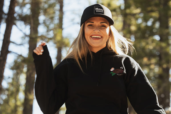 Woman wearing a black snapback hat with a white MCREY MOTOCROSS CO. logo on the front