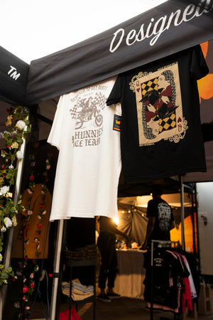 T-Shirts on display under a black canopy with 'Designed to get dirty' text at an outdoor event.