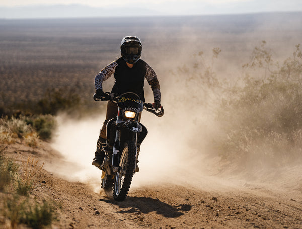 Woman riding a dirt bike in the desert with animal print sleeves 