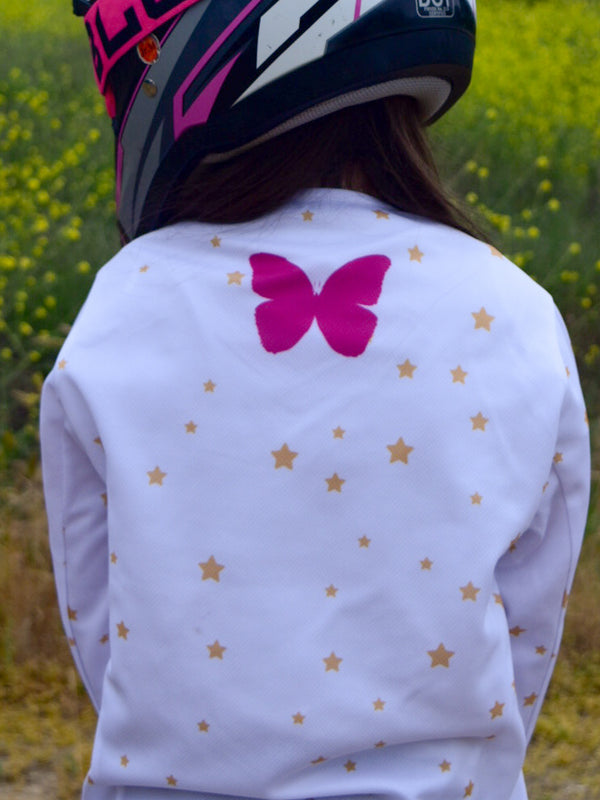 A girl wearing a white dirt bike jersey with stars and a pink butterfly on the back.