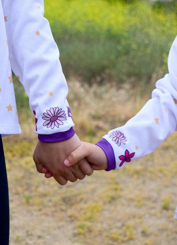 Two sisters holding hands. They are wearing white jerseys with ink and purple flowers around the sleeve.