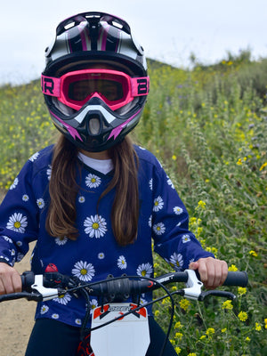 Girl sitting on a dirt bike wearing a navy blue jersey with white daisies on it.