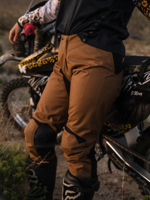 Pair of mocha and black women's dirt bike pants, leaning up against a dirt bike.