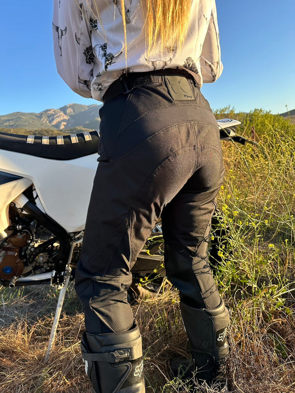 Woman standing in front of her dirt bike wearing womens black dirt bike pants and a white bull skull jersey