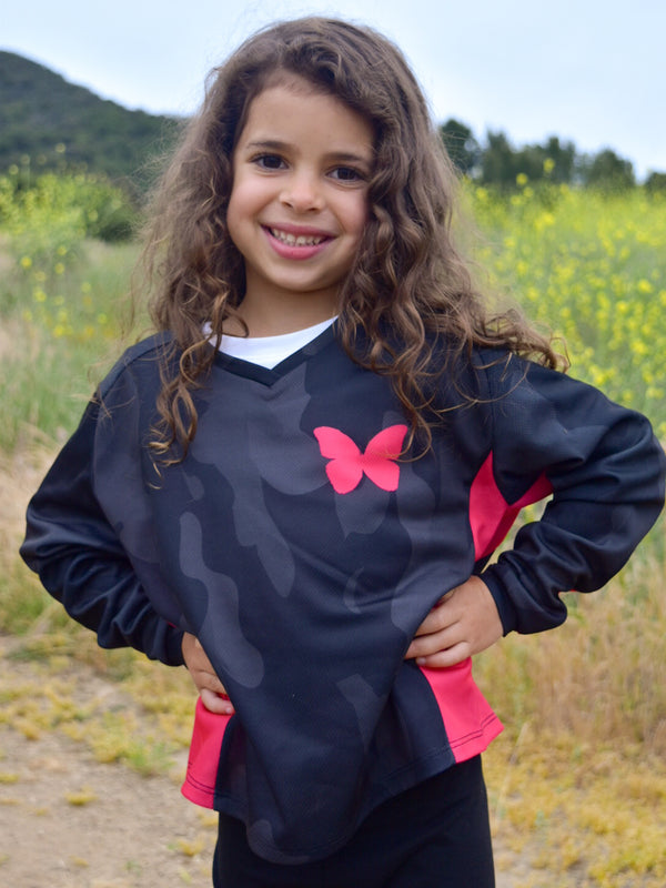 A girl wearing a grey and black camo jersey with neon pink accents and a neon ipnk butterfly on the front.