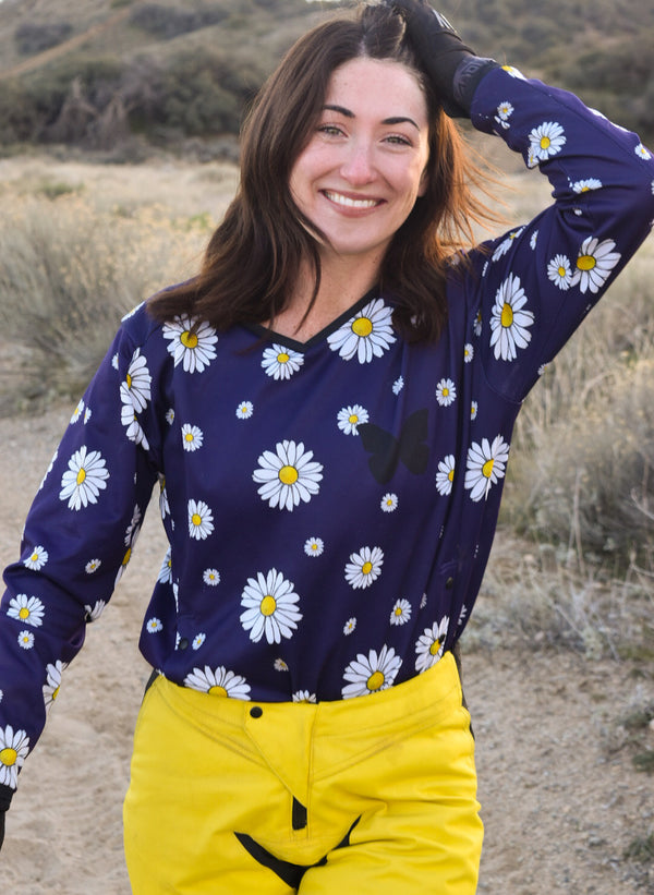 Woman wearing a navy blue dirt bike jersey with white daisies on it and bright yellow dirt bike pants. 