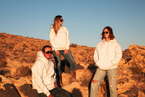 Three friends standing on a rock in the desert while the sun is setting. They are wearing unisex hooded sweatshirts with MCREY MOTOCROSS CO logo on the front.
