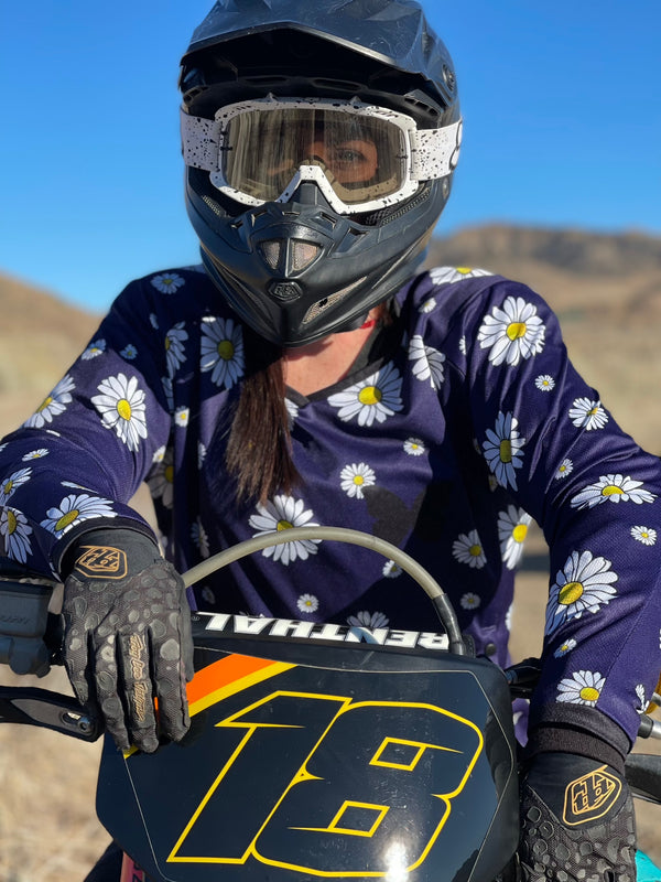 Woman sitting on a dirt bike wearing a navy blue jersey with white daisies