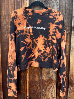 Women's cropped crewneck sweatshirt. It's black with bleach tie-dye. It says "designed to get dirty." on the front.
