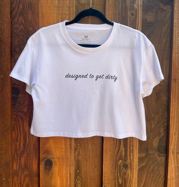 Women's white crop shirt with the words 'designed to get dirty' written in black cursive across the front.