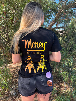 Blonde woman wearing a black shirt with two girls sitting on motorcycles standing in front of a tree